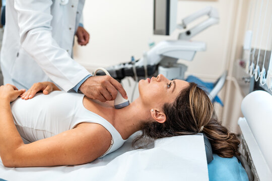 Doctor performing a thyroid ultrasound scan on a female patient lying on an exam table in a clinic. Medical professional using a transducer probe for diagnostic imaging of the neck and glands.