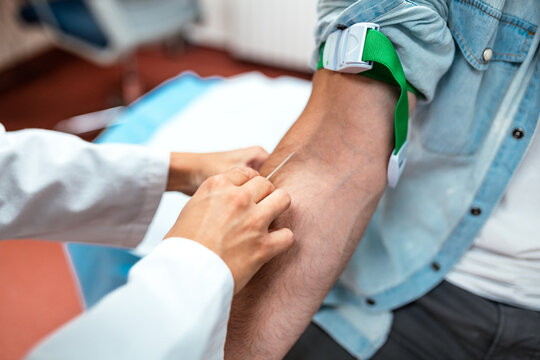 Close up of a doctor performing a blood draw on a male patient. Professional phlebotomist inserting a needle into a vein with a green tourniquet. Healthcare, medical procedure, and laboratory concept.