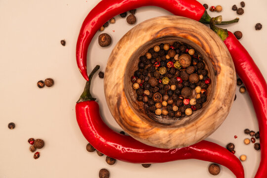Vibrant red chili peppers and a wooden mortar filled with peppercorns create a spicy culinary composition