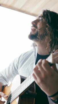 Talented male musician with long curly hair emotionally playing a classical acoustic guitar. Close up of a singer performing a song