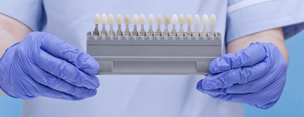 Dentist hands holding tooth shades guide for teeth whitening and professional prosthetic selection.