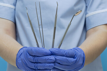 Dentist in blue gloves holding basic dental examination instruments: mirror, probe and tweezers.