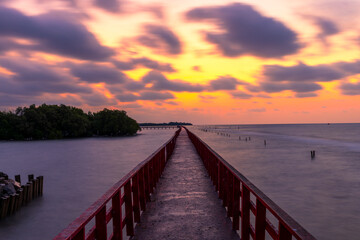 Fototapeta premium Sunset over Red Bridge with Birds Flying over the Sea at Bang Pu,A breathtaking sunset view at the Red Bridge, a famous landmark in Bang Pu, Thailand. The golden sky is filled with seagulls and birds 