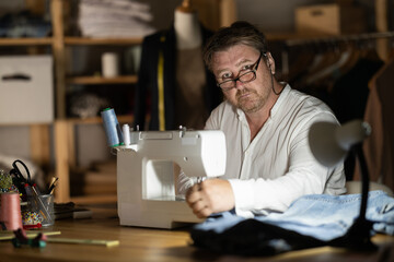 Fototapeta premium Middle-aged male dressmaker working with sewing-machine at night