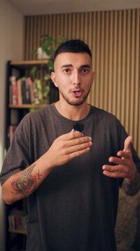 Young male content creator with tattoos speaking directly to the camera. Expressive man holding a wireless lavalier microphone for an interview