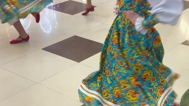 Close-up of girls in national Slavic dresses with bright flowers and white shirts in red shoes dancing on the tiled floor. The concept of Slavic dances, costumes and customs, entertainment events