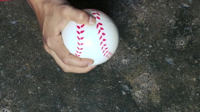 Hand gripping baseball on rough ground, close-up sports concept, tension, competition, practice shot