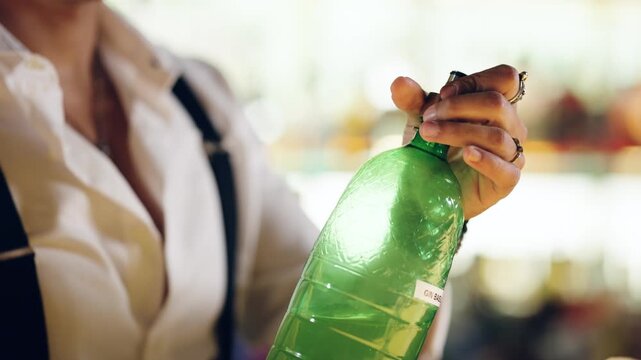 Bartender's hands opening a green bottle of gin to prepare a cocktail. Professional mixologist working at the bar counter in a nightclub