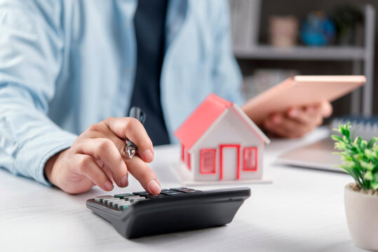 man hands using calculator with house model and tablet on desk. Concept of real estate investment, home loan mortgage, property insurance and housing finance planning.