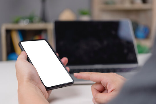 man hand holding smartphone with blank white screen mockup at home office. Male pointing finger at empty mobile phone display for app presentation. Technology copy space concept.
