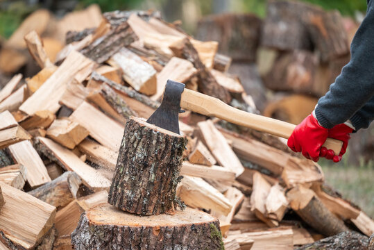Process of splitting firewood with an axe in the yard. Close-up of an axe hitting a log, chopping firewood against a large pile of timber representing strength and preparation