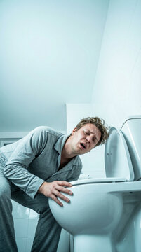 Person in pajamas leaning over a toilet, experiencing vomiting, in a brightly lit bathroom with white tiles and clean, modern fixtures