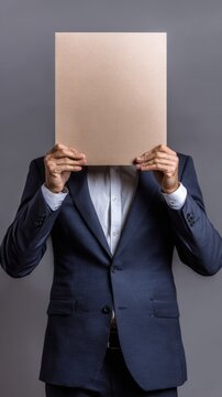 Businessman holding blank cardboard in front of face against gray background