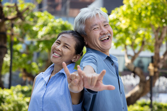 Happy laughing Asian senior couple pointing up love and peace, ILY, rock hand sign