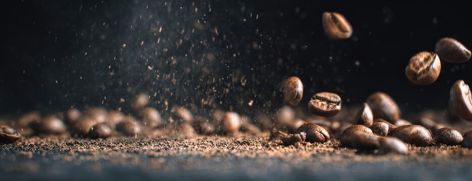 Close-up of roasted coffee beans falling and scattering on a dark surface with a blurred background.