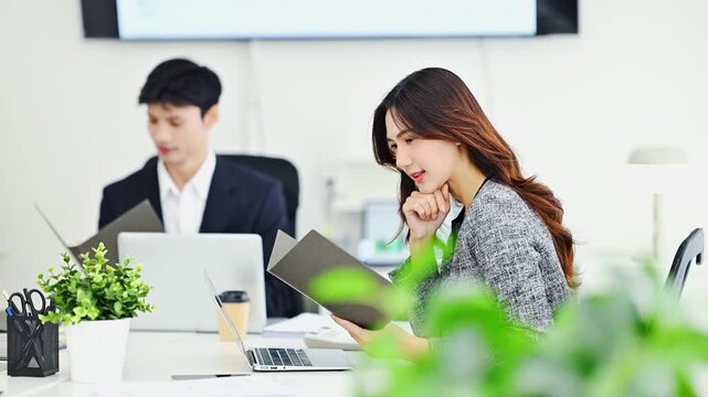 Asian business team discussing documents during a meeting in modern office. Businessman explaining paperwork to female colleague while working together with laptop and financial reports. Teamwork, cor