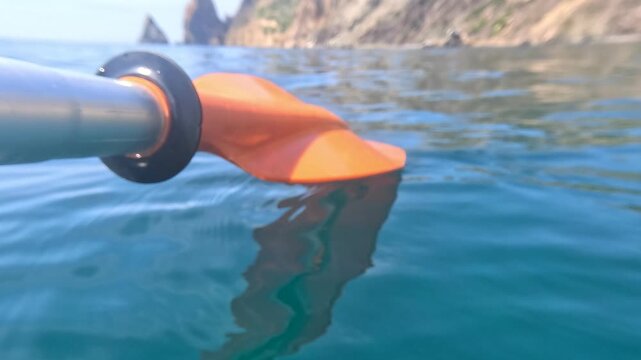 Kayak paddle ocean surface close up over turquoise water near scenic rocky cliffs during a peaceful summer adventure