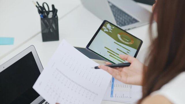Close up of businesswoman calculating financial data with calculator and tablet at office desk. Budget planning and expense analysis concept with charts and digital report.
