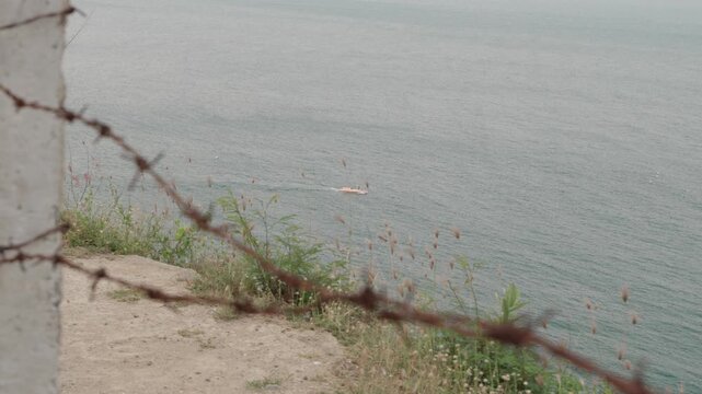 Barbed Wire Fence Overlooking Restricted Coastal Border Zone with Distant Patrol Boat