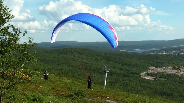 Sportsman paraglider caught the wind on the hillside summer day. 
