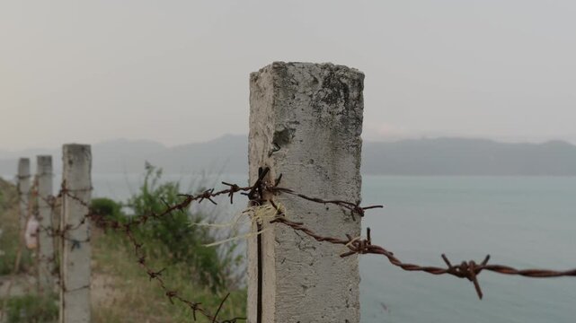 Rusty Barbed Wire Fence on Concrete Posts Overlooking Coastal Border Zone