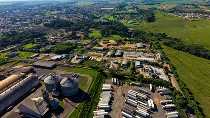 An aerial view of a large industrial complex surrounded by green fields and a cityscape in the distance. © Felippe Lopes