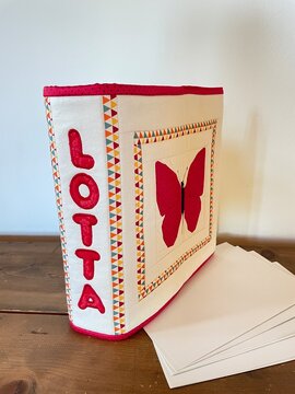 Handmade personalized quilted photo album ring binder with red butterfly appliqu&eacute; using. FPP ( foundation paper piecing)  technique and embroidered name 'Lotta' on a wooden table 