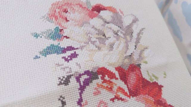 Woman hand cross-stitching a colourful floral pattern on a white canvas.