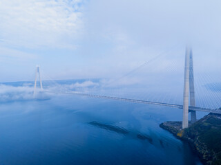 Fototapeta premium Wide aerial view of Yavuz Sultan Selim Bridge above the clouds in Istanbul. Modern suspension bridge pylon and cables through heavy fog. Ethereal Bosphorus landscape at Poyrazkoy. Atmospheric drone ph