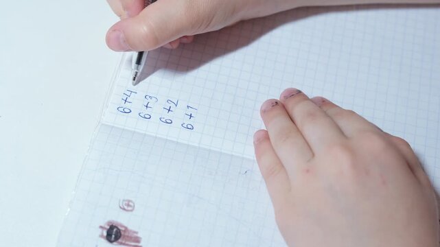 Close-up of a child's hands writing simple arithmetic exercises in a notebook, learning basic math during homework
