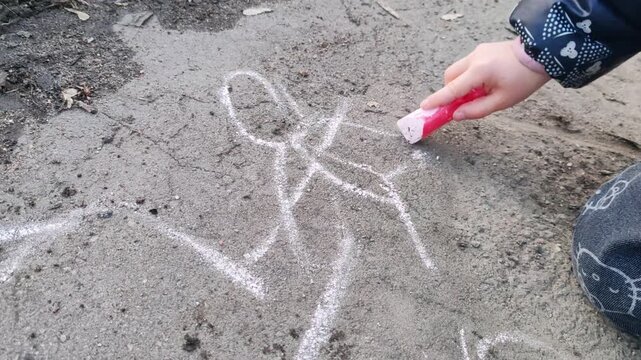 Child drawing a winged figure with chalk on asphalt, close-up of hand creating a fairy or angel on the ground during outdoor play