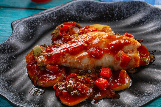 Baked fish fillet with tomato sauce and vegetables on a rustic blue wooden table