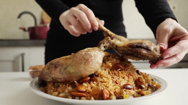 muslim woman in black hijab plating roasted chicken pieces over spiced rice with almonds and raisins for festive home meal presentation