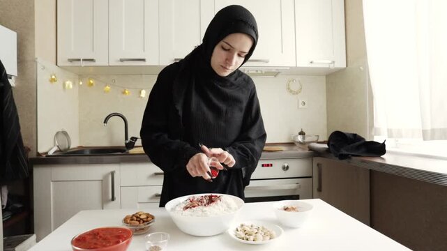 muslim woman in black hijab adds a spice blend into a large white bowl of uncooked basmati rice, preparing the base for a fragrant savory main course