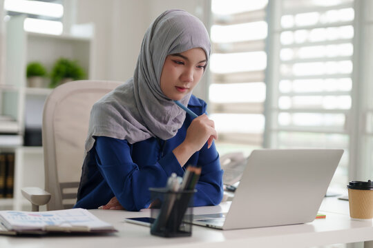 Asian Muslim woman professional remote working studying laptop business project development home office workspace contemplation research education