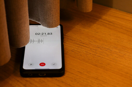 Voice detection and recording app in mobile phone listening to conversation placed on the floor near window curtains. Secretly grabbing and wiretapping inside home or apartment during covert operation