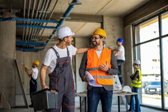 Construction supervisor patting a worker on the shoulder while discussing a site project.
