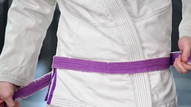 Martial arts tying kimono Gi jiujitsu karate purple belt, traditional, belt, blurred out background video, selective focus cinematic, gym setting
