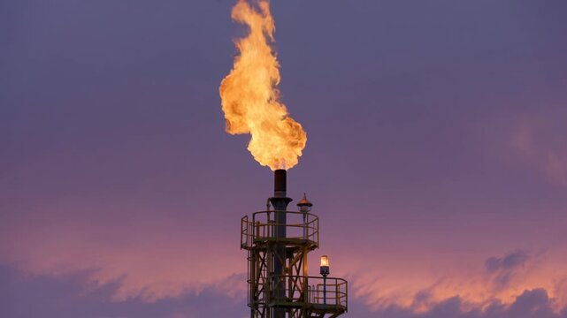 Industrial gas flare stack burns excess methane against a sunset sky to illustrate energy production and environmental carbon emissions.