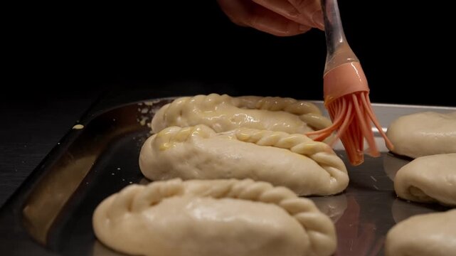 Close-up view of raw hand-crimped pastry turnovers arranged on a metal baking tray, showcasing detailed dough texture and preparation before oven baking