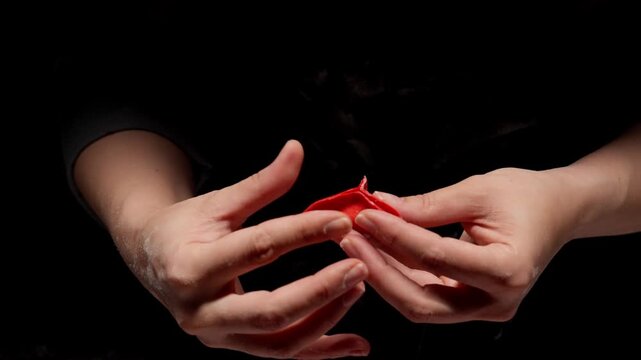 Close-up of skilled hands carefully shaping and sealing a delicate red dumpling against a dark background, highlighting precise traditional culinary craftsmanship