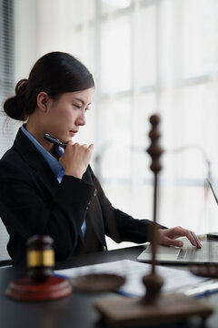 Female lawyer focusing, thinking and typing on laptop, working on a complex legal case, providing advice, studying law, and developing justice strategies in her office