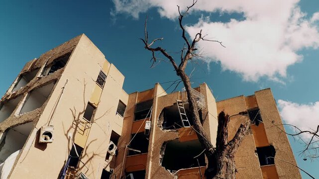 An upward facing wide angle shot, at a heavy missile falling site, during the Israel Iran war, where the buildings are broken, trees are burnt and a bird is flying across. Arad, Israel.