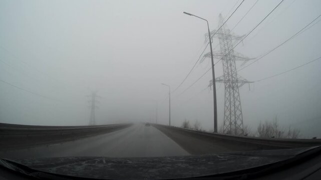 A car drives slowly along a foggy road past electrical poles. Driver point of View.