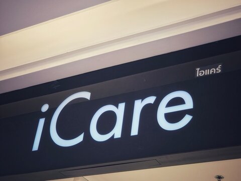 Low-angle view of the illuminated iCare logo in white on a black storefront sign with Thai script on April 5, 2026 in Bangkok, Thailand.
