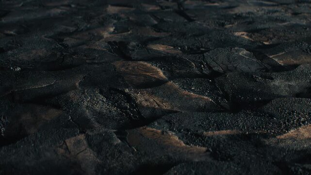 Charred cracked earth surface with wavy textured pattern in dramatic lighting on dark background, concept of erosion and resilience