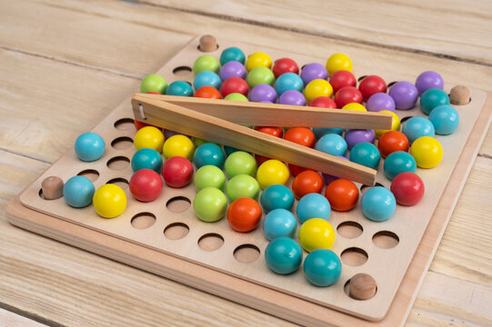 Colorful wooden balls on game board with holes, wooden tweezers picking up balls, bright and playful scene showcasing children educational toy, vibrant colors and fun. child play by montessori