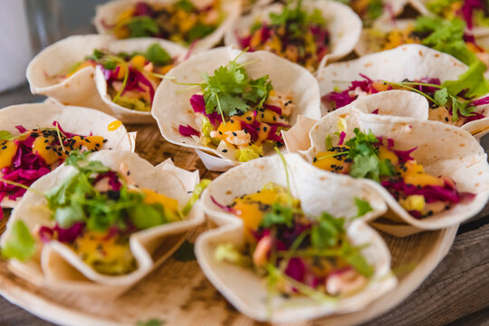Delicious mini fish tacos served as appetizers, featuring vibrant red cabbage, fresh mango salsa, black sesame seeds, and cilantro garnish on small soft tortillas at a professional catering event.