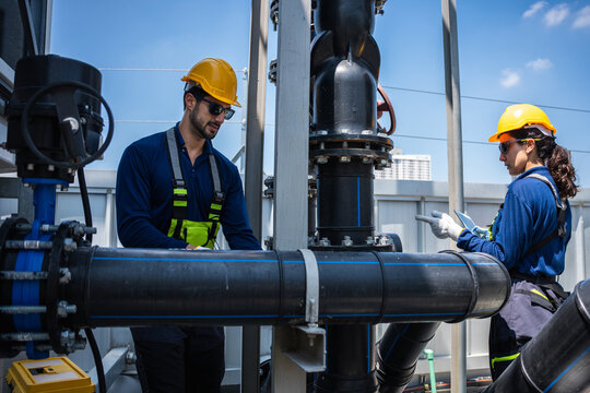 Industrial engineers in safety gear inspecting large water pipe system at treatment plant, Professional team of technicians monitoring industrial plumbing with digital tablet