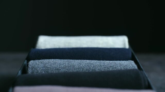 New box of neatly rolled men socks in various colors on table, with camera focus changing reveal each pair, highlighting soft cotton textile, style variety. Colorful rolled cotton socks in black box